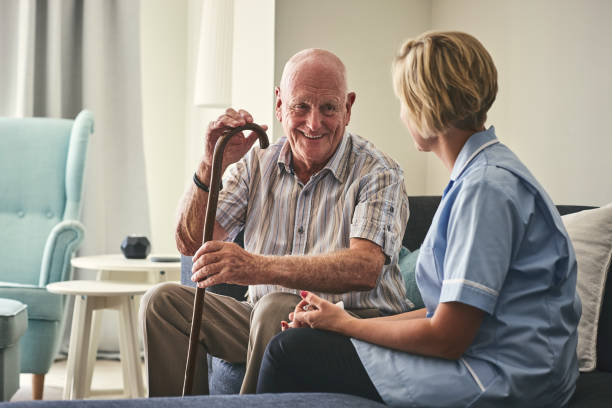 Smiling retired senior man sitting on sofa with female home carer at care home